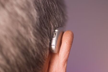 Caucasian white old aged man wearing modern digital hearing aid in ear with grey hair.の写真素材