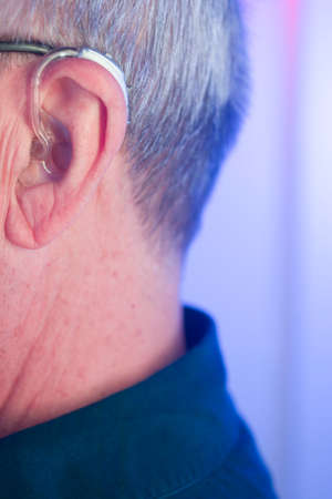 Caucasian white old aged man wearing modern digital hearing aid in ear with grey hair.の写真素材