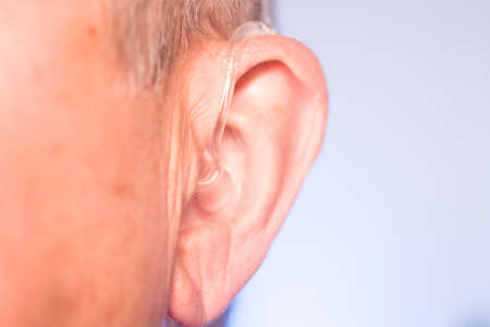 Caucasian white old aged man wearing modern digital hearing aid in ear with grey hair.