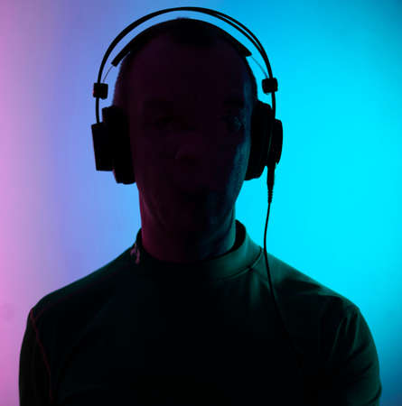 Dj deejay electronic wearing music headphones with coloured lights plain studio background.