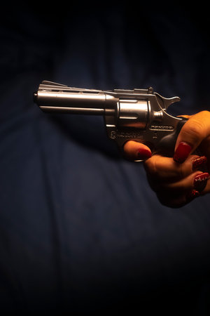 Lady spy detective with painted red nail varnish holding pistol gun at nightの写真素材