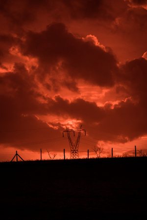 Apocalypse cloudscape suggesting a horror scene. Fiery red landscape with backlit power pylon.の写真素材