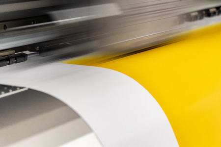 Big professional large scale printer, processing a deep yellow glossy sheet of paper for color...