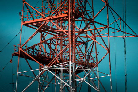 Engineering progress for communication structures. Massive, red and white power pylon on blue sky,...