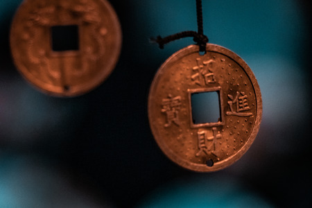 Orinetal, magical pendants. Traditional asiatic and chinese currency, transformed into fortune coins with handmade engravings. Bronze, copper, gold necklace, black thread, blurry blue background.の写真素材