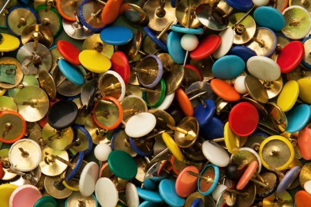 Background texture of a variety of multi colored drawing pins / tacks.