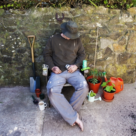 Male gardener, bare feet, grubby and asleep in garden chair amongst his tools after gardening の写真素材