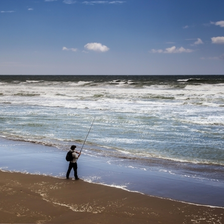 Fisherman fishing at the tide on the beach with wild sea の写真素材