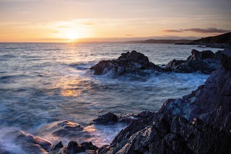 Inspiring and dramatic sea view, sunset over the ocean and waves surging over rocks, Cornwall, UK. Long exposure.の写真素材