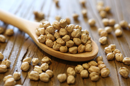 Dry and uncooked chickpeas in spoon and scattered on wooden backgroundの写真素材
