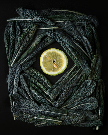 Green Tuskan Kale leaves end lemon slices on a dark background. Healthy detox vegetables. Clean eating and dieting concept. Top view. Health kale benefitsの写真素材