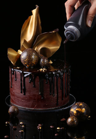 Fancy chocolate cake, isolated, black background, studio. The hand of the pastry chef is present in the frameの写真素材