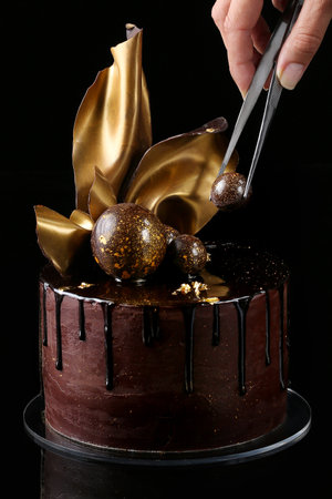 Fancy chocolate cake, isolated, black background, studio. The hand of the pastry chef is present in the frameの写真素材
