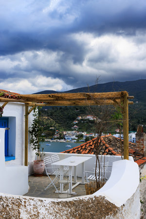 Whitewashed houses, red roofs, and scenic sea view under dramatic sky in Poros, Greece.の写真素材