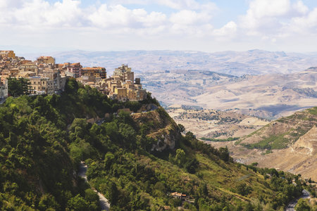 Panoramic view of Enna, Sicily, Italy. The hilltop town surrounded by mountains and valleys, showing historic architecture and winding roads under a clear summer sky.の写真素材