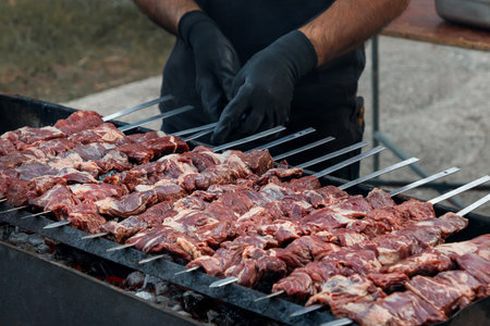 Raw meat skewers on barbecue grill with chef hands