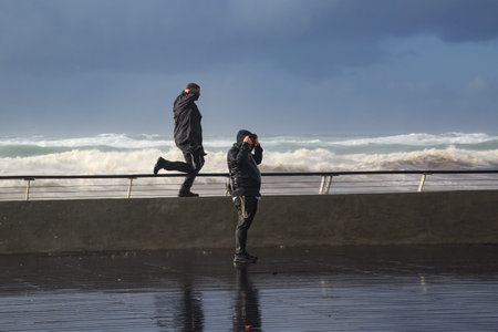TEL AVIV, ISRAEL - January 03, 2018: Two people on wet promenade during violent winter storm with massive waves on Tel Aviv seafront