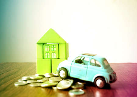 Home wooden block with car and coin on wooden table and white background, with pastel light