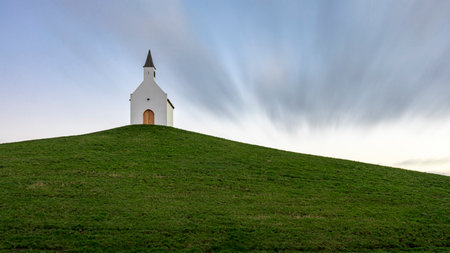 A Small white church on top of a grassy hill. It's a long exposure shot on a partly clouded day.の写真素材