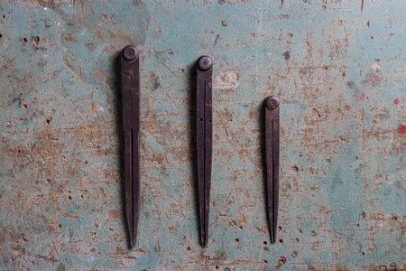 Three metal compass dividers for woodworking on a rustic surface flat lay top viewの写真素材