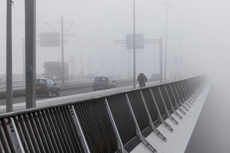 Rotterdam, the Netherlands - 2021-10-08: Erasmus bridge in Rotterdam in the fog with traffic driving in poor vissibility conditionsのeditorial素材