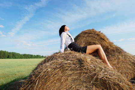 Woman on hay bale in summer field enjoying a warm windy dayの写真素材