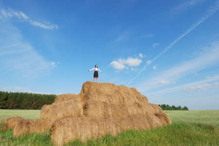 Woman on hay bale in summer field enjoying a warm windy dayの写真素材