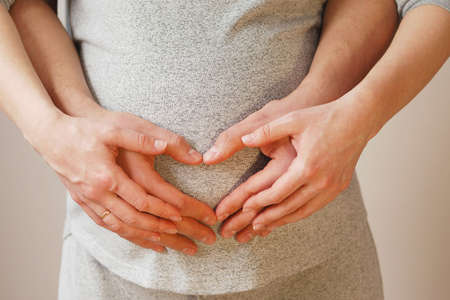 Hands of young couple showing heart on belly of pregnant wifeの写真素材