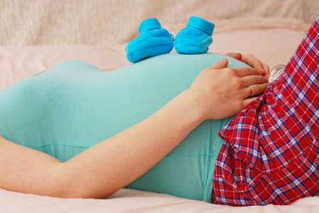 Pregnant woman lying with baby shoes on her stomach in last month of pregnancyの写真素材