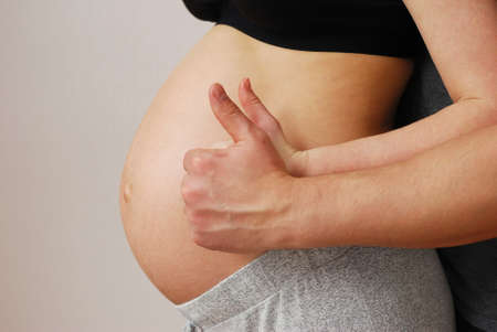Hand of happy young parents showing OK sign on background of stomach of wife on last month of pregnancyの写真素材