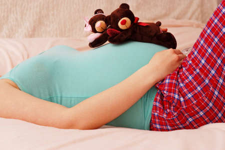 Young pregnant mother lies with soft toy of their future baby on last month of pregnancyの写真素材