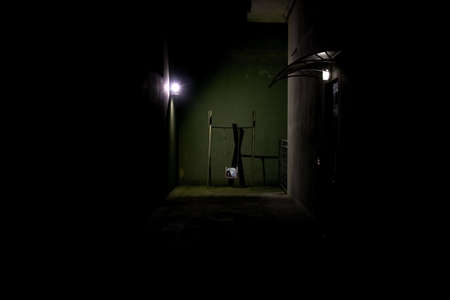 A swing at the end of an alley. A dark alley and a light source shining on the swing.の写真素材