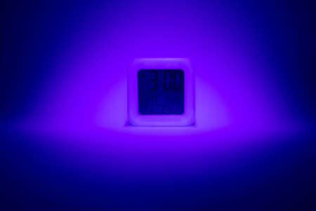 A digital alarm clock showing 3 o'clock. Stylized background with specific lighting in the colors of blue and purple.の写真素材