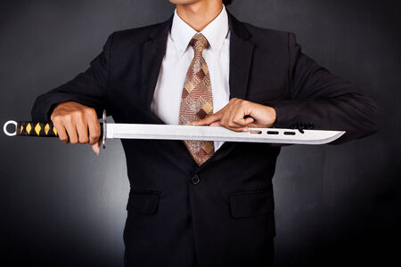 Young determined businessman in suit holding swordの写真素材