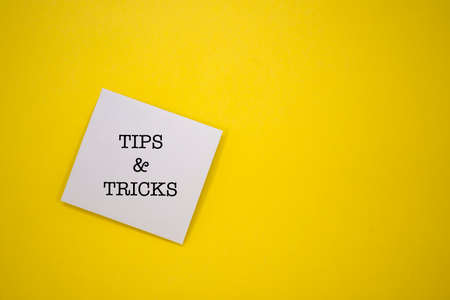 The words Tips & Tricks written on a sticky note on a yellow background.