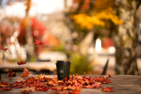 Coffee cup on wooden table with autumn leaves in the background