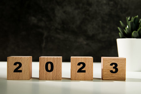 Wooden blocks with numbers 2023 on white table and black wall background