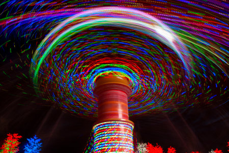Carnival amusement park ride with swings. Spinning fair ride at night with bright purple, red, green and yellow lights.の写真素材