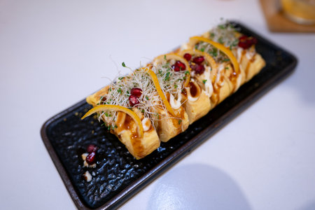 Tasty rolls with cheese and pomegranate seeds on a black plateの写真素材