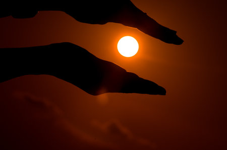 Silhouette of hand holding the sun in the sky background.の写真素材