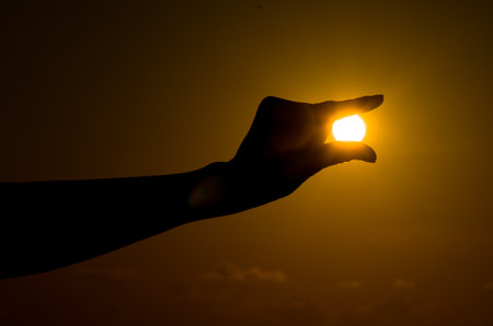 Silhouette of hand holding the sun at sunset background. (Selective focus)の写真素材