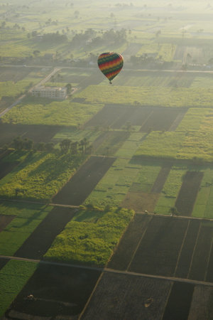 Hot Air Balloon Soaring Over Egyptian Farmlands at Sunrise, Showcasing Lush Green Fields and the Serene Rural Landscapeの写真素材