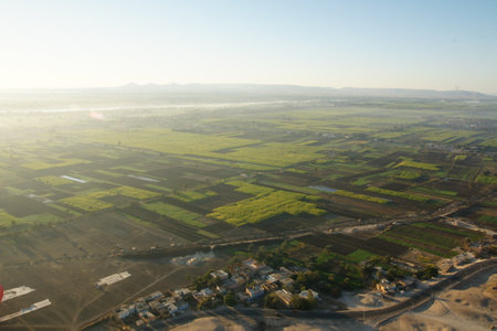 Hot Air Balloon Soaring Over Egyptian Farmlands at Sunrise, Showcasing Lush Green Fields and the Serene Rural Landscapeの写真素材