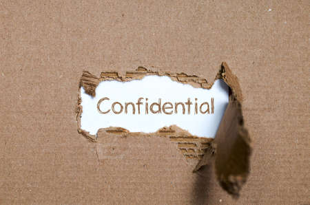The word Confidential appearing behind torn paper.の写真素材