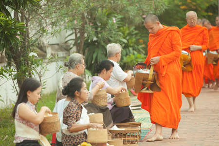 People giving alms to buddhist monks on the street, Luang Prabang, 20 JUNE 2014のeditorial素材