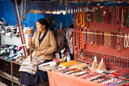 Dharamsala, India - 28 September, 2014: Tibetian woman praying with traditional hand prayer wheel at the street market, Dharamsala, India.のeditorial素材