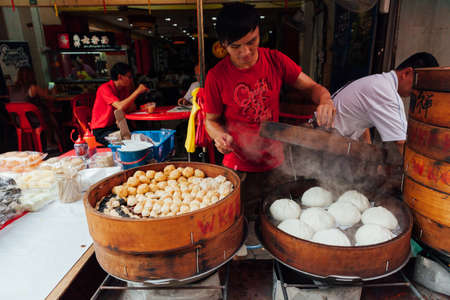 Kuala Lumpur, Malaysia - March 17, 2016:  Young man cooking chinese traditional steamed buns at the street food stall in Chinatown, Kuala Lumpur, Malaysia on March 17, 2016.のeditorial素材