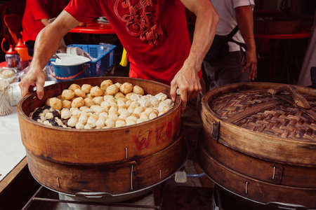 Kuala Lumpur, Malaysia - March 17, 2016:  Young man cooking chinese traditional steamed buns at the street food stall in Chinatown, Kuala Lumpur, Malaysia on March 17, 2016.のeditorial素材