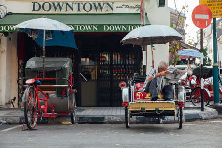 George Town, Malaysia - March 21, 2016: Rickshaw reading a newspaper sitting on the tricycle at the street of the  George Town, Penang, Malaysia on March 21, 2016.のeditorial素材