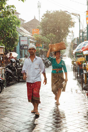 Ubud, Indonesia - March 08, 2016: Indonesian man and woman in traditional clothes walking under the rain on the street of Ubud, Bali, Indonesia on March 08, 2016のeditorial素材